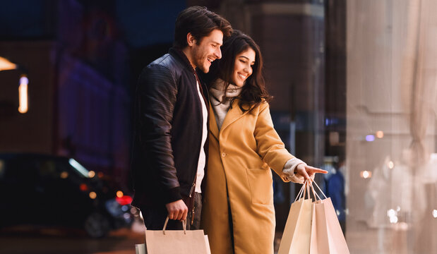 A couple standing in front of a store, holding shopping bags filled with purchases.