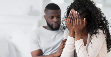 A woman is crying while her partner comforts her. She is covering her face with her hands and he is putting his arm around her.