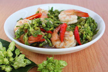 Stir fry shrimp with green telosma cordata flowers and place red chilli slices on top. in a white porcelain plate Fresh flowers on the wooden table