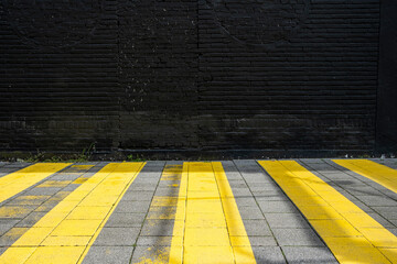 Stark contrast between bright yellow pedestrian crossing lines on a dark textured brick wall in Rotterdam, creating a bold urban composition