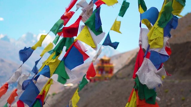 Slow motion shot of colorful Tibetan Buddhist prayer flags waving in front of the Gue Monastery in Spiti Valley, Himachal Pradesh, India. Prayer flags in front of the monastery in India.	