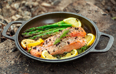 Healthy baked salmon steaks with greens and asparagus in a black cast iron skillet. A delicious...
