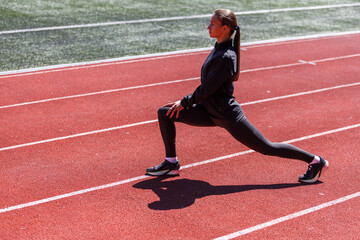 Young runner woman stretching her legs after training at the stadium