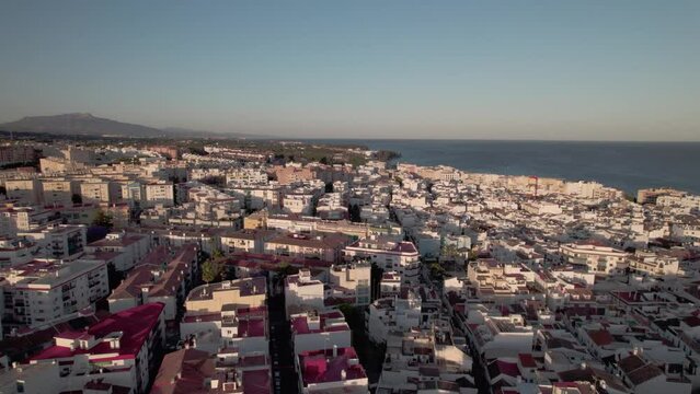 Aerial view of coastal town with mountains, white buildings, ocean, beach, and waterfront