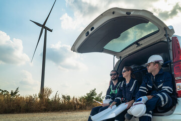 A team of engineers sitting in a van is inspecting the construction of a wind turbine and...