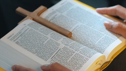 Bible book with cross place between book page while placed the book at prayer laps. Represented...