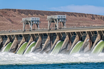 The waters of the Columbia River rush through the spillway gates below the cranes at the McNary Dam...