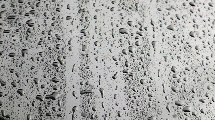 This image captures raindrops on a dark surface, highlighting their glistening clarity and natural beauty.