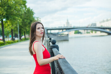 Obraz premium A woman in a red dress stands on a bridge overlooking a pond. She looks into the distance, perhaps lost in thought. Loneliness and contemplation concept