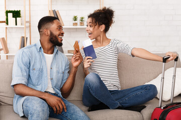 African American man and woman are sitting side by side on a comfortable couch, surrounded by their luggage. They appear to be preparing for a trip, with bags at their feet