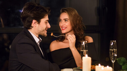 Romantic beautiful European couple having dinner in restaurant, feeding each other, enjoying delicious food