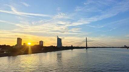 A large city with tall buildings and parks spread out on the riverbank. Wave on the water. A bridge...