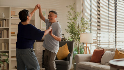 Fototapeta premium asian senior happiness couple home isolation concept,asian old retired adult couple dancing together at living room with cheerful and joyful moment ,Lovely senior couple dancing at home