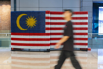 A men walk past the Malaysian flag made out of plastic bottle. Jalur Gemilang for Independence Day or Merdeka Day celebration and Hari Malaysia.