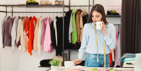 A woman is standing in front of a table, holding a cup of coffee. She appears to be pausing to...
