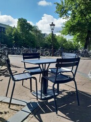 Cafe tables and chairs on a street corner in Amsterdam. Old lamp post and bridge over the canal.
