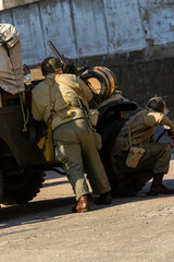 Historical reconstruction. An American infantry soldiers from the World War II  prepare to attack hidden behind a milirary vehicle. View from the back