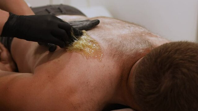 Beautician in black gloves epilating male back with Sugaring. Male beauty treatment, The process of waxing in a beauty salon
