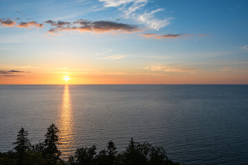 Sunset over the Baltic Sea. Evening blue sky and beautiful clouds in different tints of red and yellow. A sunny path, a glare on the water surface from the horizon to the wooded shore