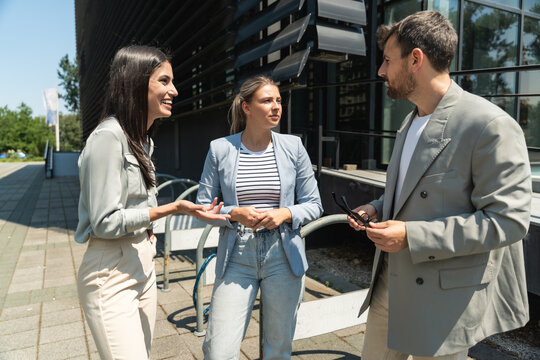 Group of young successful business people, businessman and businesswoman standing out of office building in formal wear, discussing about business. Cool happy expatriate company experts exchange info
