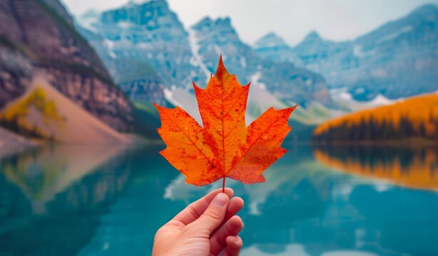 The hand of a man holding an orange maple leaf. A traditional Canadian autumn landscape with a lake and mountains. Canada Day concept, copy space. - Powered by Adobe