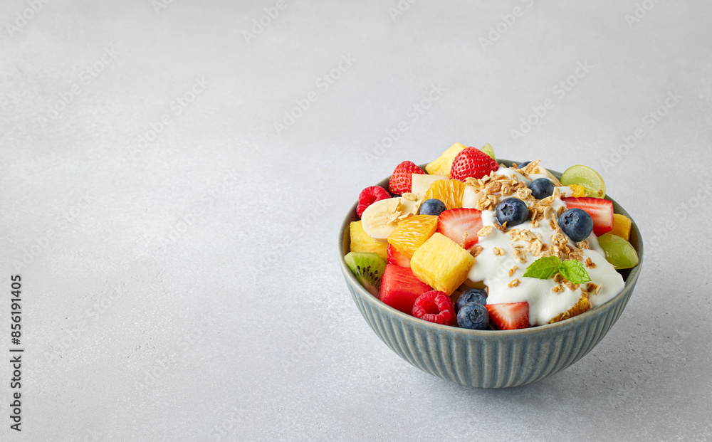 Poster bowl of fresh fruit salad, muesli and greek yogurt on gray background - Posters