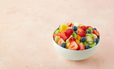 Bowl of fresh fruit salad, muesli and greek yogurt on light pink background