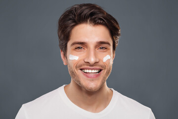 Obraz premium Care about appearance. Positive man with cream on cheeks smiling at camera
