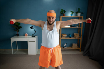 Happy active man in orange fitness outfit doing exercise at home. He doing exercises with dumbbells, to fitness
