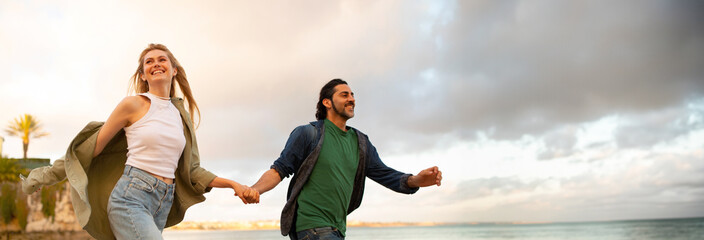 A young couple walks hand-in-hand along a beach at sunset. They are both smiling and seem to be...