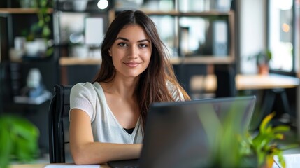 Fototapeta premium Portrait of a young woman in a modern office, seated at a desk with an empty laptop screen, engaged in digital marketing planning, representing her professional management and communication abilities