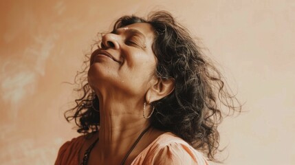 Fototapeta premium A woman with closed eyes smiling wearing a necklace and earrings with her head tilted back against a textured beige background.