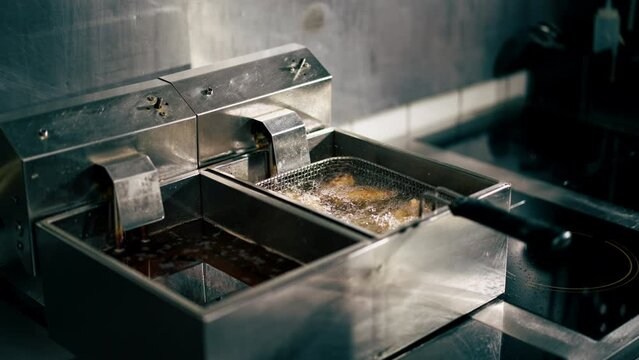 close-up in a professional kitchen frying chicken wings in oil in a deep fryer