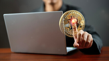 An Asian man is displaying a gold Bitcoin intricately held on her right fingertip pointing upwards on a gray background, symbolizing the concept of cryptocurrency.