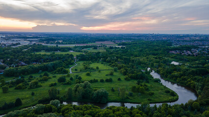 Aerial view of a suburban area with industrial buildings and city skyline in the background under a soft evening sky with gentle clouds.