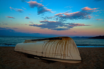 A fishing boat on a beach. An old fishing boat lying overturned on a beach at sunset 
