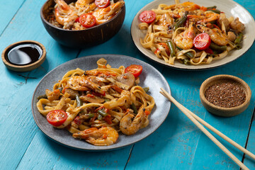 shrimp udon and rice in shrimp pad thai sauce on a blue table next to soy sauce and chopsticks