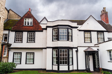 Charming historic cottage with white walls and black trim, featuring unique bay windows and a quaint garden. Perfect for showcasing traditional English architecture and serene residential charm.