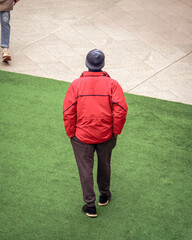 Urban solitude captured as an individual in a red jacket stands contemplatively on green turf...