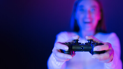 A woman is shown holding a video game controller in her hands, her fingers positioned to press the buttons. The controller is connected to a gaming console or computer, copy space © Prostock-studio