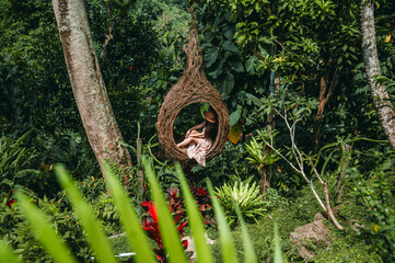 A female tourist is sitting on a large bird nest on a tree at Bali island, Indonesia
