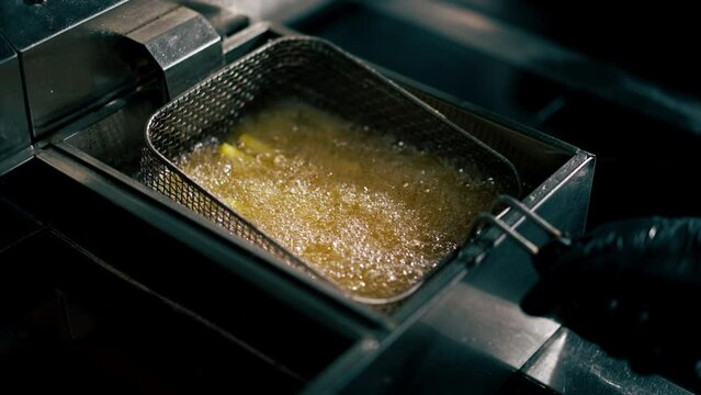 close-up in professional kitchen frying French fries in oil in a deep fryer chef shake it