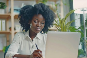 Focused black businesswoman taking notes during online meeting.