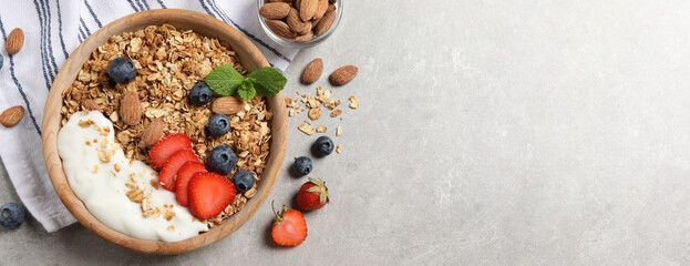 Tasty granola with blueberries, strawberry, yogurt and almonds on grey table, top view. Banner design with space for text