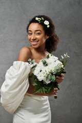 A beautiful African American bride in a white wedding dress holds a bouquet of white flowers.