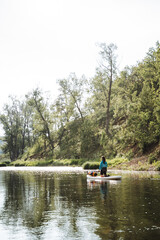 In a peaceful setting, someone is enjoying paddle boarding on a serene river surrounded by the beauty of nature, with water, sky, and trees harmoniously blending in the landscape