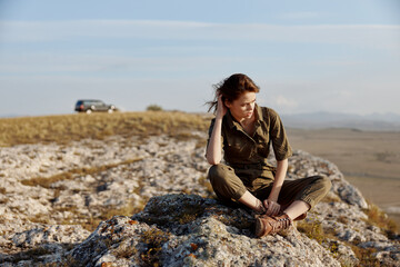 Woman sitting on rock with car and mountains in background a traveler's serene escape amidst nature's beauty