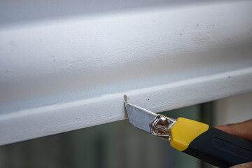 A man uses a utility knife to remove paint. Knife yellow-black