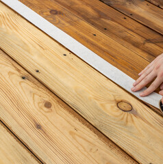 A hand is applying painters tape to a wooden surface, creating a clean line for a future paint project.