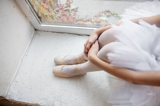 Close up ballet pointe shoes. Ballerina dancer sits by the window, pose relaxed, with pointe shoes on and the soft tulle of tutu, evoking moment of tranquility.